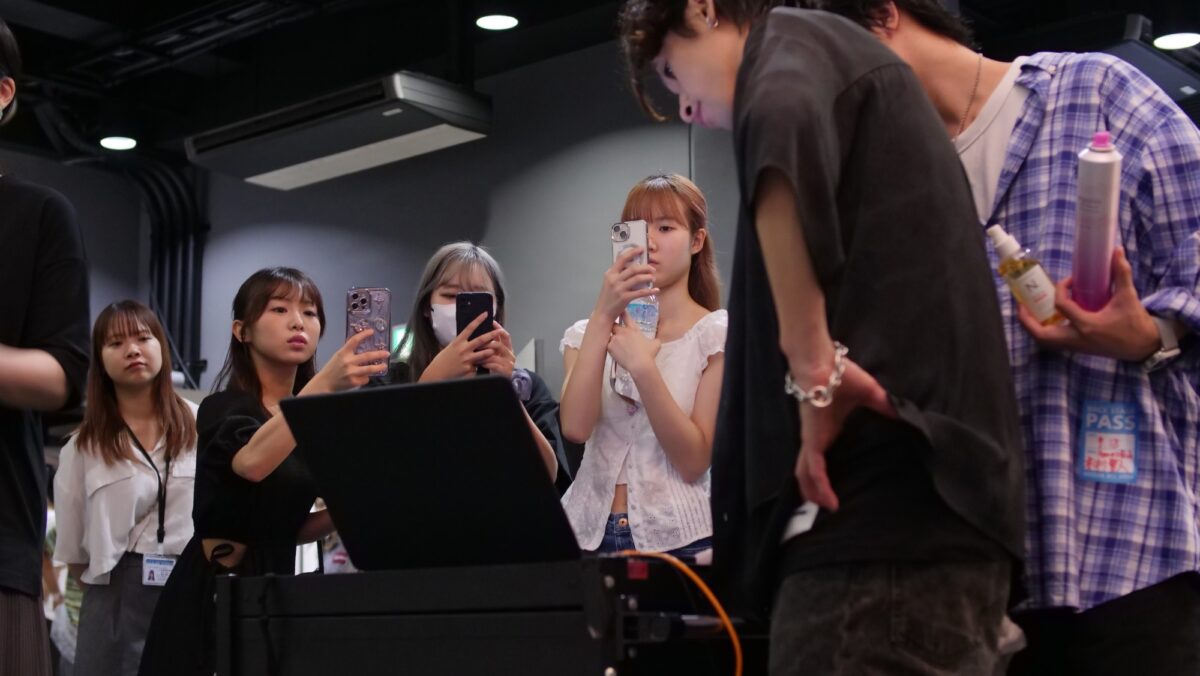 美容専門学校の撮影授業でスタイリストの手元をスマートフォンで撮影する学生たち